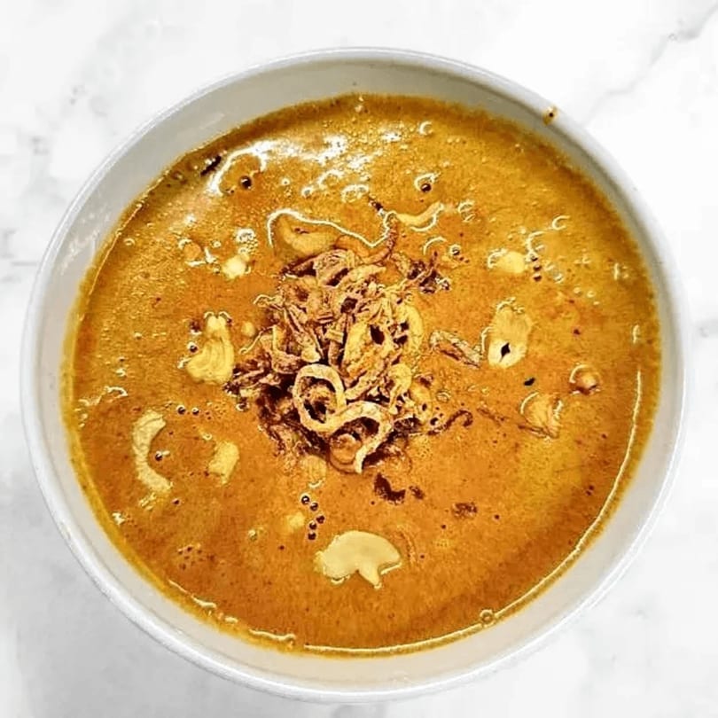 Close-up of a bowl of Red Jasmine Thai curry, topped with crispy fried onions.