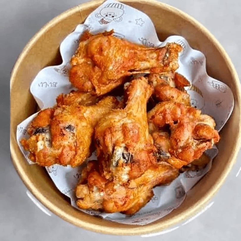 Golden-brown fried chicken drumsticks and wings in a brown bowl lined with white patterned paper.