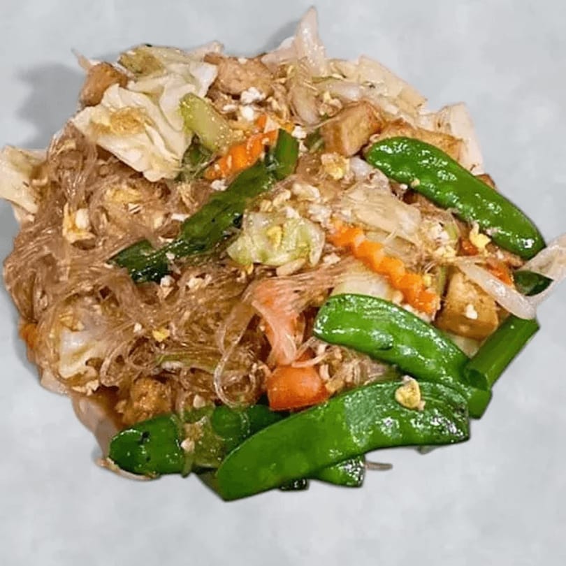 Thai glass noodle stir-fry with snow peas, carrots, cabbage, and tofu on a white plate.