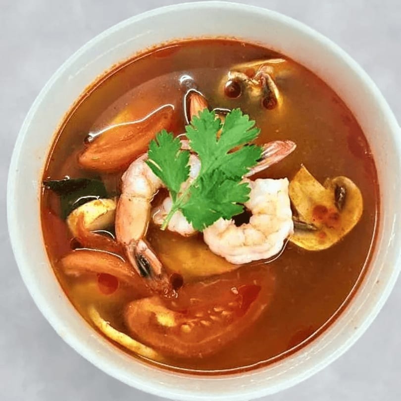 Red Jasmine Thai Tom Yum soup with shrimp, mushrooms, tomatoes, and cilantro in a white bowl.