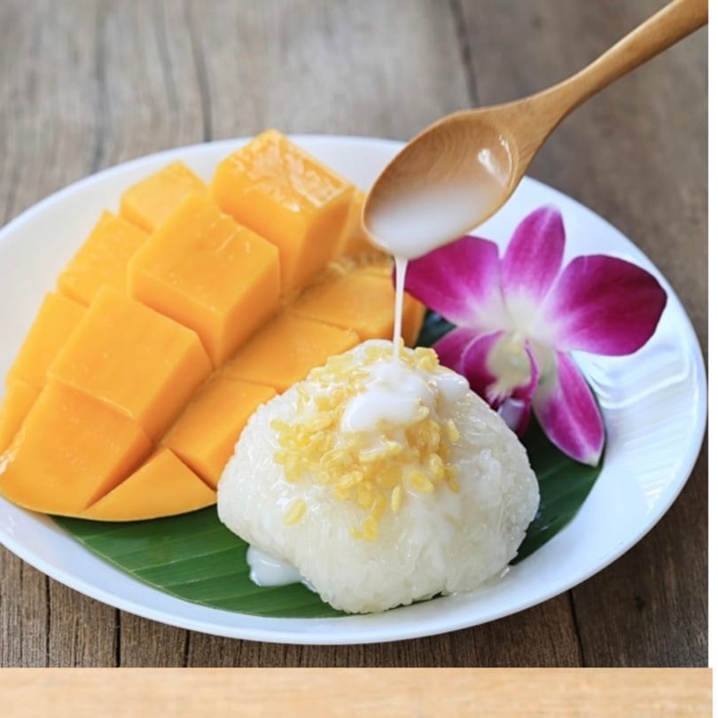 Mango sticky rice with coconut milk being poured over it, garnished with an orchid.