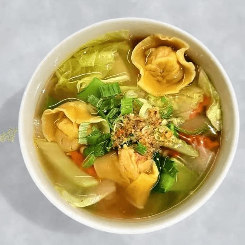 A bowl of Thai wonton soup with green onions, cabbage, and crispy garlic.