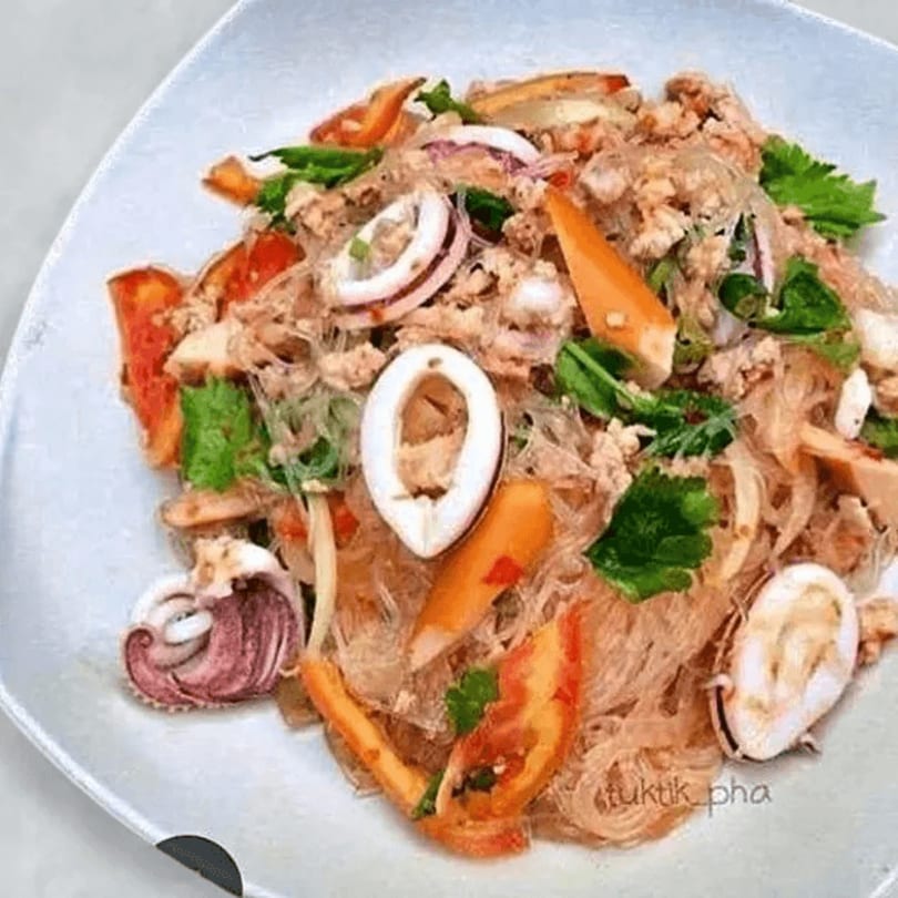 Thai glass noodle salad with squid, ground meat, red onions, tomatoes, and herbs on a white plate.